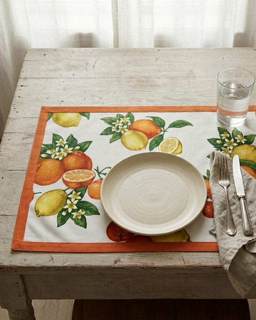 Table setting with a decorative placemat featuring citrus fruits on a wooden table.