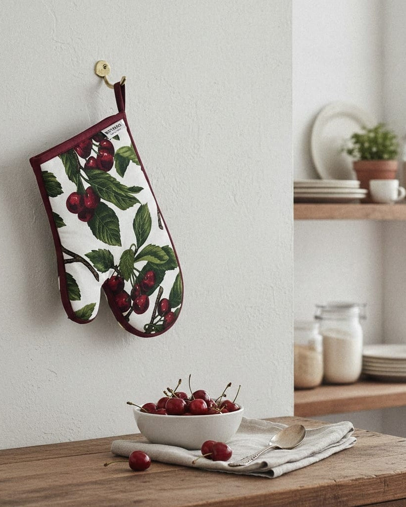 Oven mitt with cherry design hanging on a wall next to a kitchen counter with a bowl of cherries.
