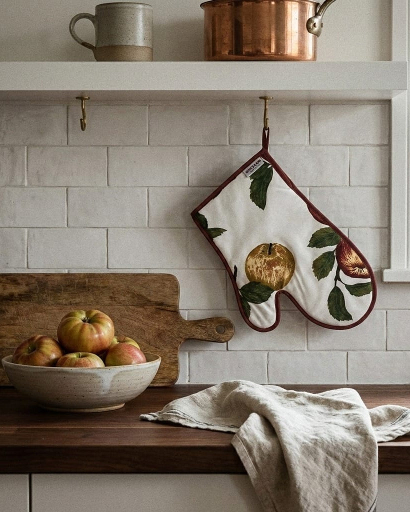 Kitchen scene with a bowl of apples, wooden cutting board, and embroidered pot holder.