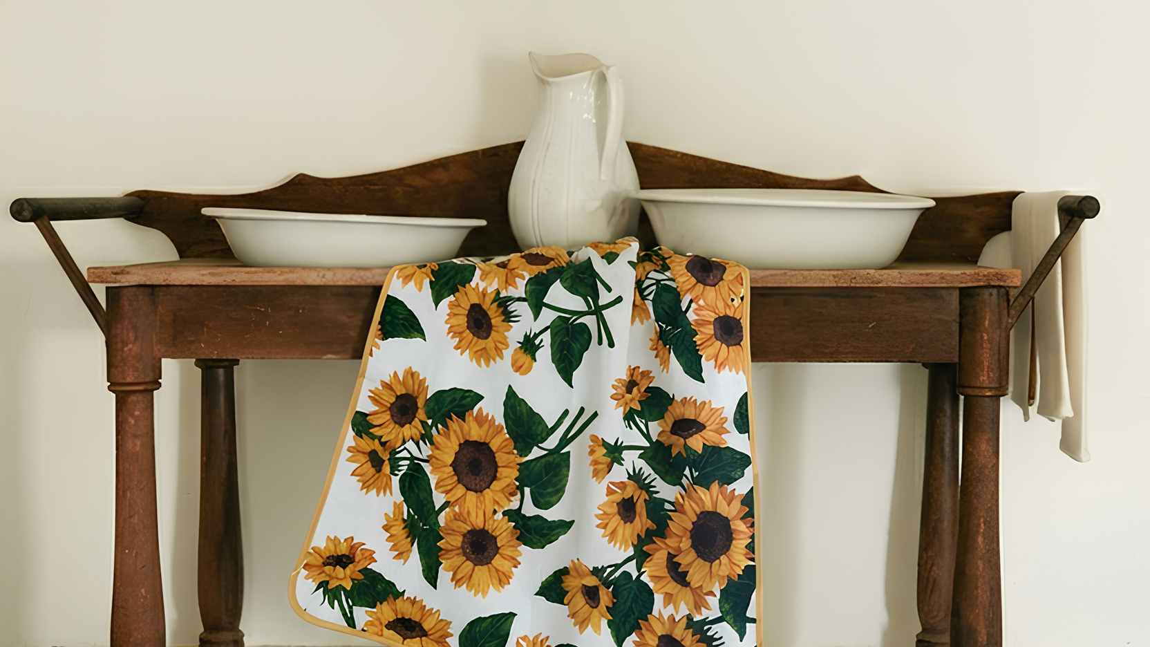 Wooden table with a floral towel draped over it against a white wall with two small mirrors.